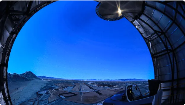 Flight simulator with blue sky and runway projection on domed screen.